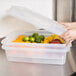 A person holding a Vollrath Traex food storage container with fruit in it.