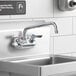 A Krowne Silver Series wall-mount faucet with lever handles and a 10" swing nozzle above a stainless steel sink.