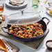 A Staub dark blue enameled cast iron brazier with food in it and a glass lid.