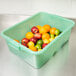 A Vollrath Traex green food storage box filled with fruit including oranges, a lemon, and a red apple.