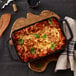 A Staub black enameled cast iron rectangular baking dish with cheese and basil leaves on top.