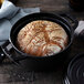 A round loaf of bread in a black Staub enameled cast iron pot.