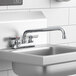 A Krowne deck-mount faucet with lever handles and a swing nozzle above a stainless steel sink.