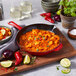 A Staub enameled cast iron skillet with shrimp and vegetables on a table.