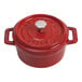 A Staub cherry red enameled cast iron mini Dutch oven with a lid and handle.