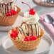A waffle bowl filled with vanilla ice cream, chocolate syrup, whipped cream, and several maraschino cherries with stems.