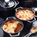 Three black Staub enameled cast iron mini Dutch ovens with food in them on a table.
