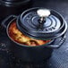 A black Staub enameled cast iron mini Dutch oven with food inside on a table.