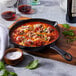 A Staub enameled cast iron skillet with meatballs, sauce, and cheese on a table in an Italian restaurant.