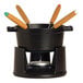 A black Staub enameled cast iron fondue pot with wooden handles and four forks.