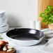 A Staub white enameled cast iron skillet with a lid on a counter with garlic and onions in it.
