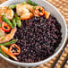 A bowl of black rice with shrimp, tomato, and asparagus.