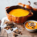 A bowl of pumpkin soup with nuts and cranberries served in a Staub burnt orange pumpkin enameled cast iron dutch oven.