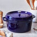 A dark blue Staub enameled cast iron pot with a lid on a table with wooden utensils.