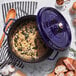 A dark blue Staub enameled cast iron Dutch oven with a lid on a table with food inside.
