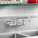 A Krowne wall-mount faucet with lever handles and a swing nozzle above a stainless steel sink.