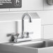 A Krowne deck-mount faucet with lever handles and a gooseneck nozzle installed on a counter above a stainless steel sink.