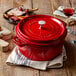 A Staub cherry enameled cast iron pot with a lid on a table with food and wine.