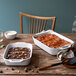 A wooden table with food in two white Staub rectangular baking dishes.