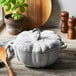A white Staub enameled cast iron pumpkin Dutch oven with a metal handle on a table with a wooden spoon.