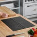 A black non-slip plastic cutting board liner placed on a wooden kitchen countertop.