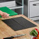 A black non-slip plastic cutting board liner placed on a wooden countertop.