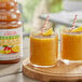 Two glasses of mango smoothie with straws on a table.