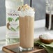A glass of brown liquid with whipped cream and coconut flakes with a straw in it.