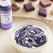 A bowl of white and purple liquid with a Chefmaster Violet Oil-Based Candy Color bottle in the background.