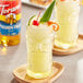 A glass of yellow drink with a cherry on top.