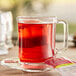 A glass mug with red liquid on a saucer with a Bigelow Cranberry Apple Tea bag.