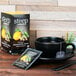 A black coffee mug with a tea bag on a black plate next to a box of Steep By Bigelow Organic Chamomile Citrus Tea.