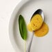 A spoon with a spoonful of yellow mustard on a plate.