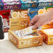 A person's hand holds a box of ONE Cinnamon Roll Protein Bars.