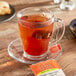 A glass cup of Bigelow orange and spice tea on a saucer with a tea bag.