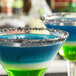 A close up of a blue drink in a martini glass with a black lava rim.