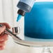 A person using a silver and blue Chefmaster airbrush to paint a cake blue.