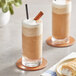 Two glasses of The Frozen Bean Spiced Chai Tea Latte with brown liquid and straws.