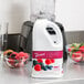 A white Torani bottle of Wildberry Fruit Smoothie Mix on a counter with bowls of berries.