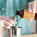 A person pouring LorAnn Oils Caramel Bakery Emulsion into a metal measuring cup.