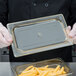 A person in gloves holding a Cambro plastic container lid over a tray of food.