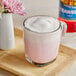 A glass cup of pink liquid with foam on top.