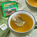 A green mug filled with yellow liquid and a Twinings Green Tea, Pomegranate, Raspberry, & Strawberry Tea bag.