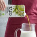 A person pouring Tazo green tea matcha concentrate into a glass pitcher.