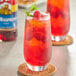 A glass of red raspberry drink with a straw and a Torani Red Raspberry syrup bottle.