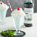 A glass of Monin mint syrup with whipped cream and a red cherry on top.