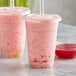 Two plastic cups with straws filled with pink strawberry smoothies.