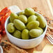 A bowl of green Cerignola olives on a wooden table.