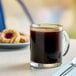 A glass mug filled with Cafe Bustelo espresso coffee on a saucer with a donut.