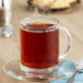 A glass mug with Bigelow Earl Grey tea on a saucer with a spoon.